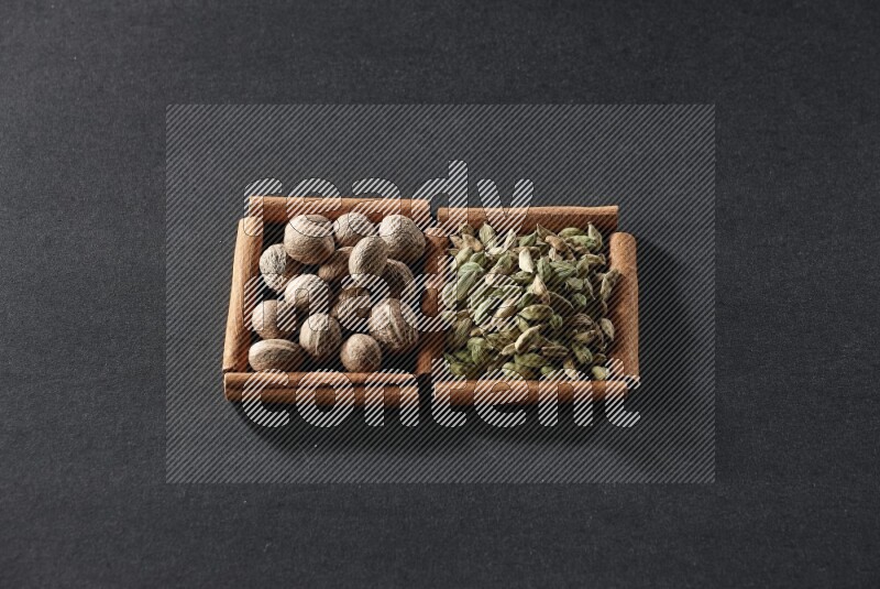 مربعان من أعواد القرفة ممتلئان بجوزة الطيب وحبوب الهيل علي خلفية سوداء