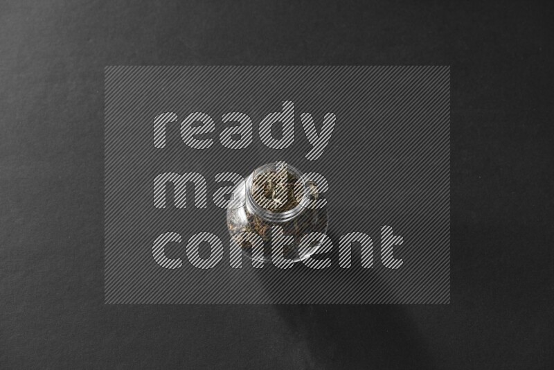 A glass spice jar full of basil on black flooring