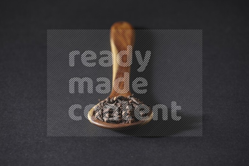 A wooden ladle full of whole cloves on a black flooring
