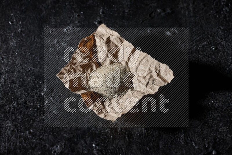 White pepper powder in a crumpled paper on textured black flooring