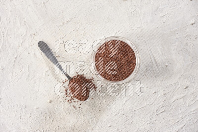 A glass jar and a metal spoon full of garden cress seeds on a textured white flooring
