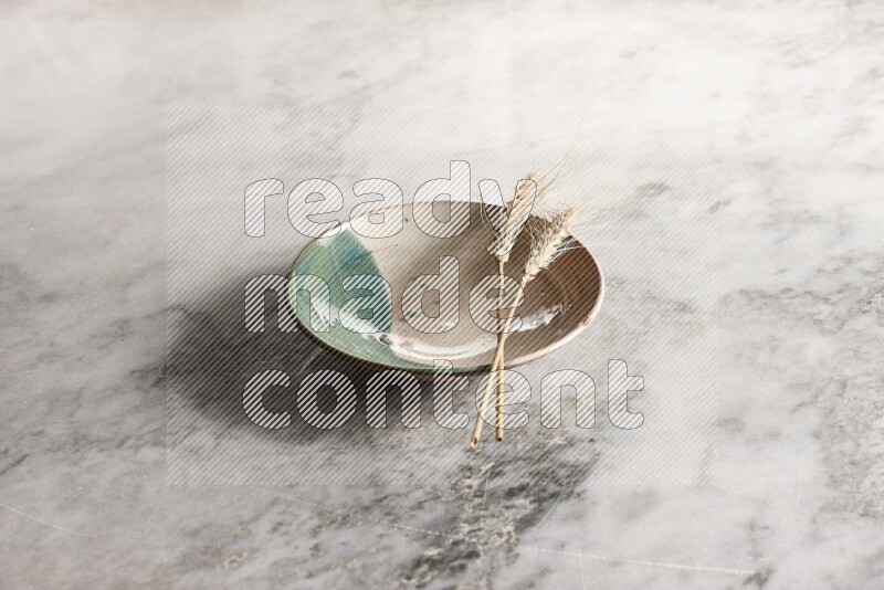 Wheat stalks on multicolored pottery plate on grey marble background