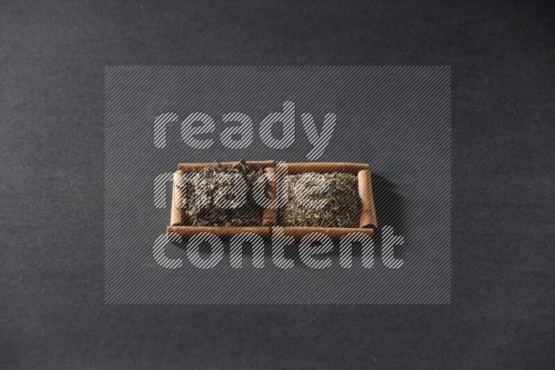 2 squares of cinnamon sticks full of cumin and dried basil on black flooring