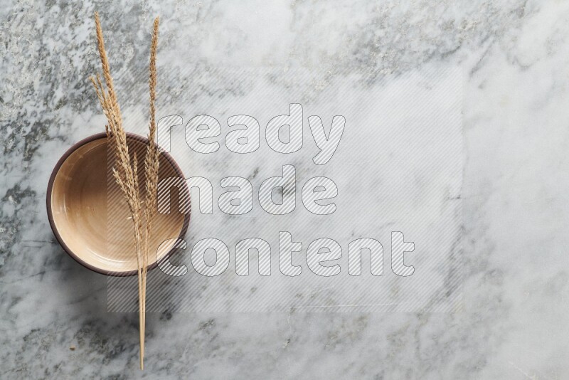 Wheat stalks on beige pottery oven bowl on grey marble background