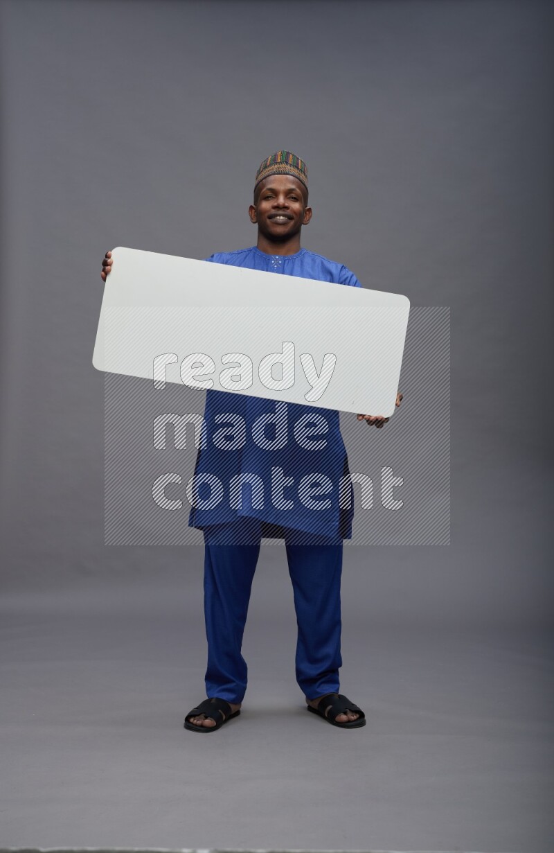 Man wearing Nigerian outfit standing holding board on gray background