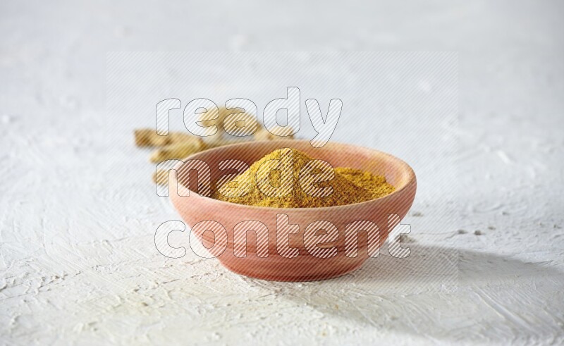 طبق خشبي ممتلئ ببودرة الكركم مع أصابع الكركم المجففة على خلفية بيضاء