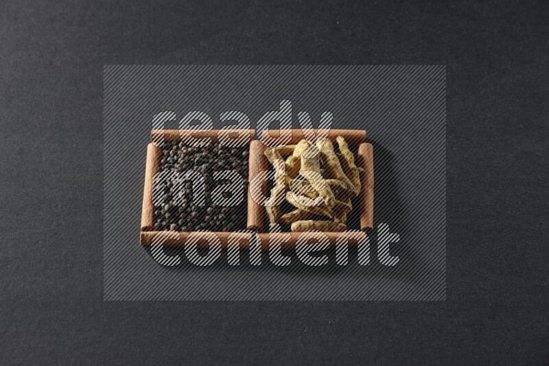 مربعان من أعواد القرفة ممتلئان بحبوب الفلفل الأسود وأصابع الكركم علي خلفية سوداء