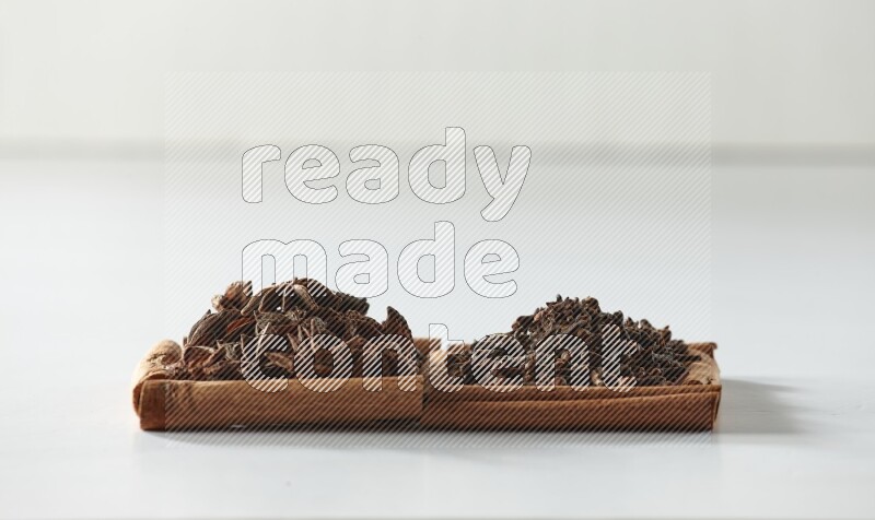 مربعان من أعواد القرفة ممتلئان بالقرنفل واليانسون النجمي علي خلفية بيضاء