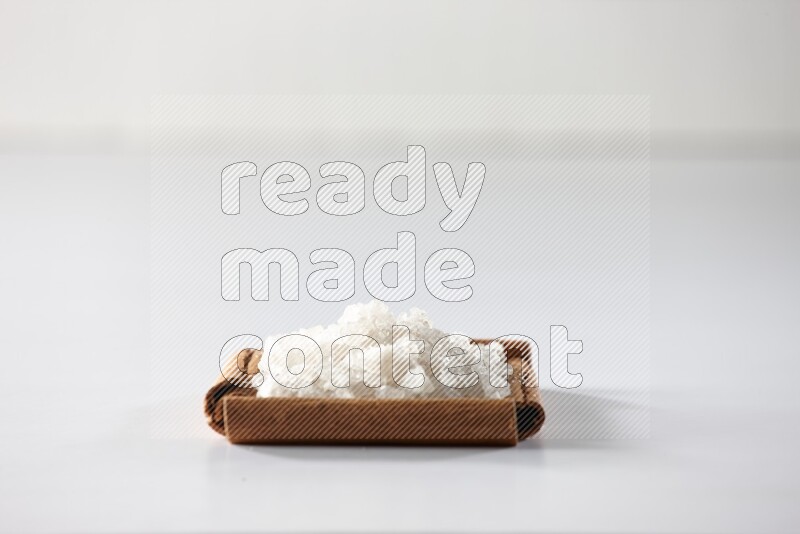 أربعة من أعواد القرفة مكونة شكل مربع بداخلها ملح أبيض علي خلفية بيضاء