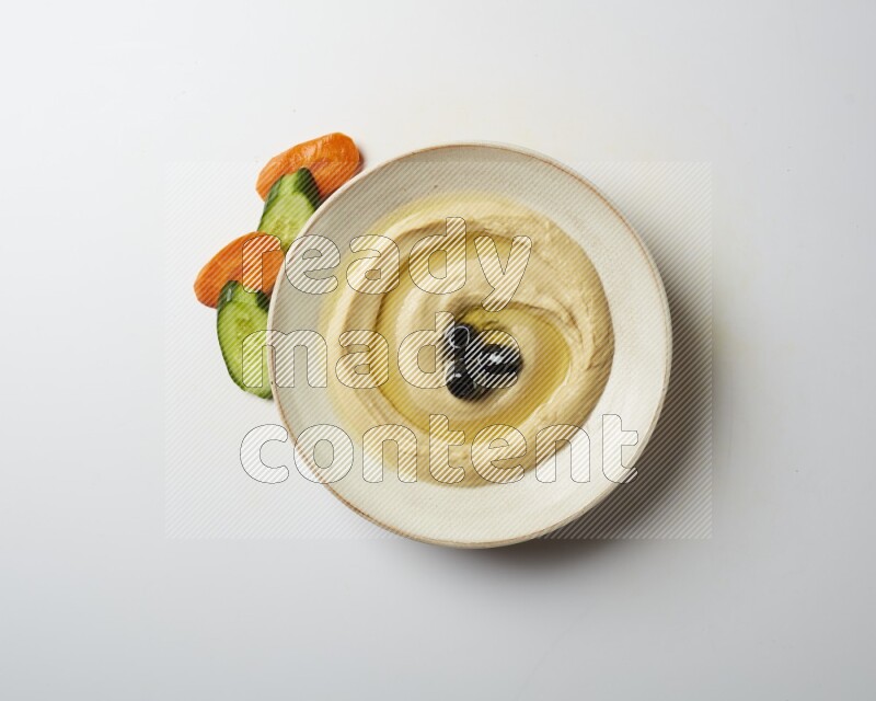 Hummus in a pottry plate garnished with black olives on a white background
