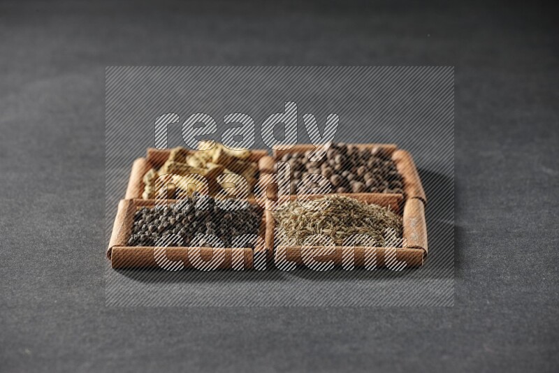 4 مربعات من عيدان القرفة ممتلئة بحبوب الفلفل الأسود والكمون وبهار الفلفل الحلو وأصابع الكركم على أرضية سوداء