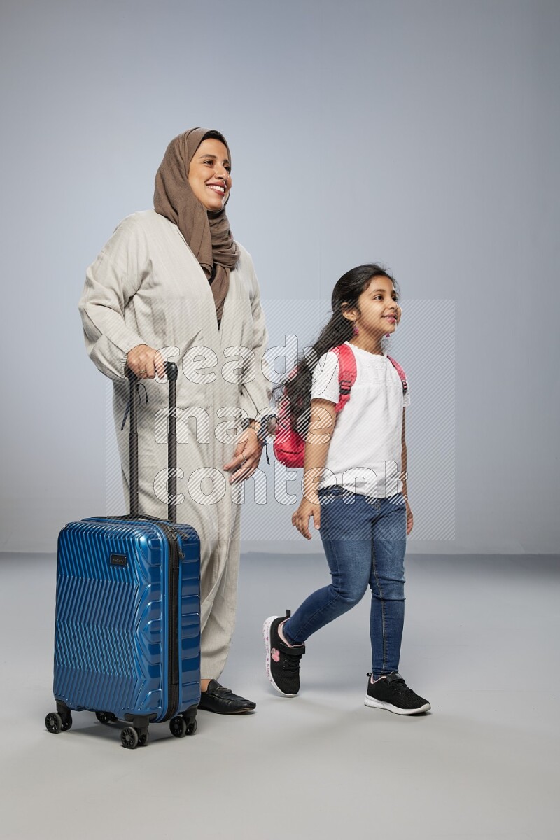 Mom and daughter standing pulling a carry-on bag on gray background