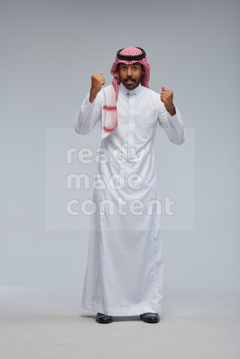 Saudi man Wearing Thob and shomag standing interacting with the camera on Gray background