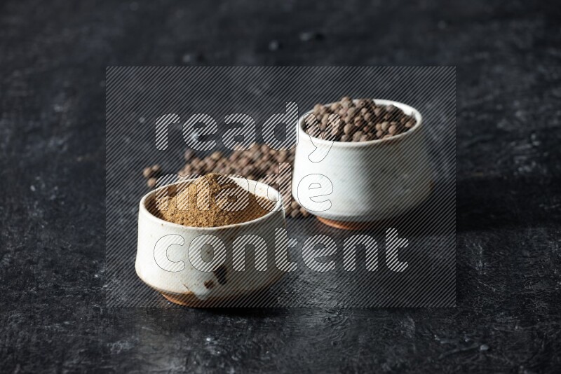 وعاءان بيج، أحدهما ممتلئ ببودرة بهار الفلفل الحلو والآخر بالحبوب وكلاهما متناثران على خلفية سوداء