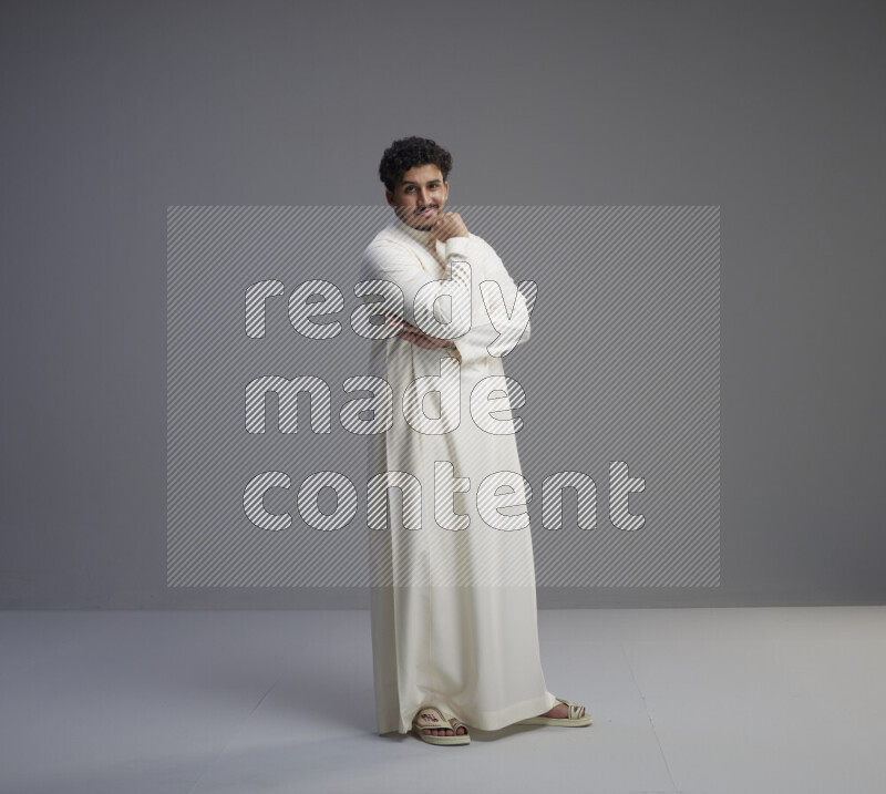 A Saudi man standing wearing thob interacting with the camera on gray background