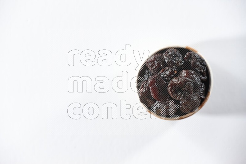 A beige ceramic bowl full of dried plums on a white background in different angles