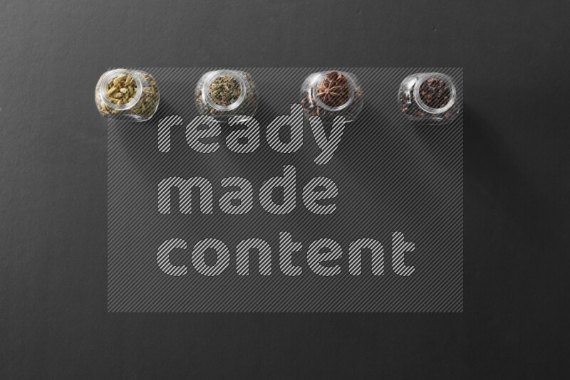 قرنفل وحبوب الهيل وريحان مجفف ويانسون نجمي في أوعية زجاجية علي خلفية سوداء