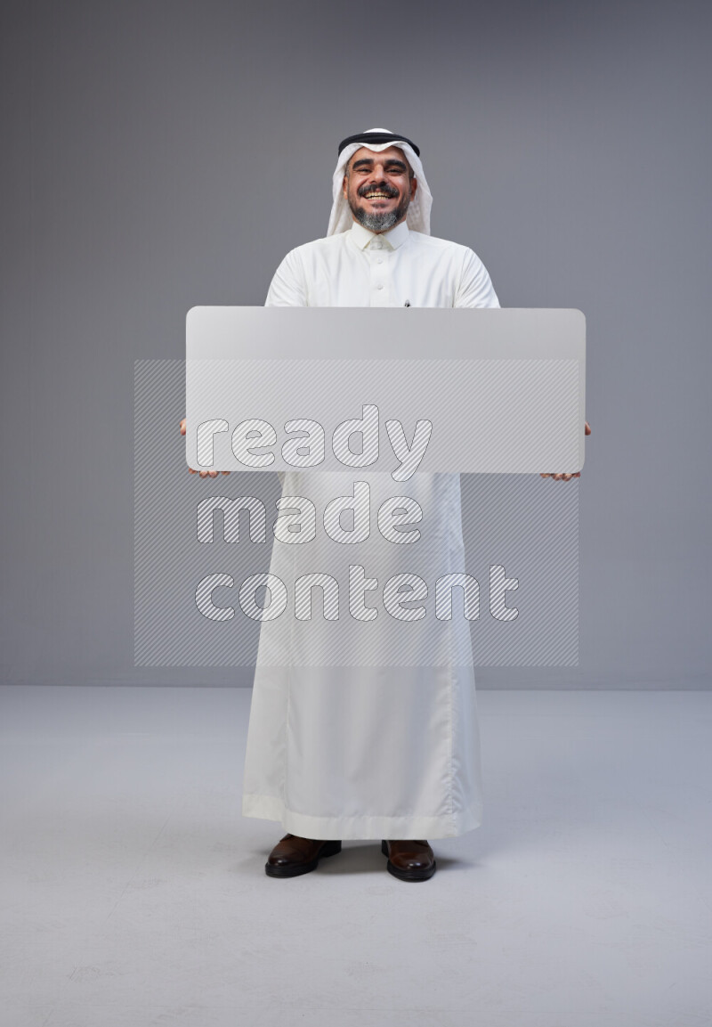 Saudi man Wearing Thob and white Shomag standing holding board on Gray background