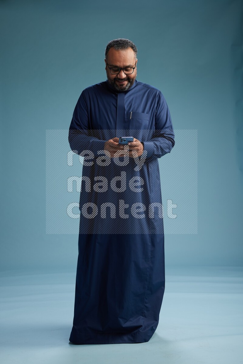 Saudi Man without shimag Standing texting on phone on blue background