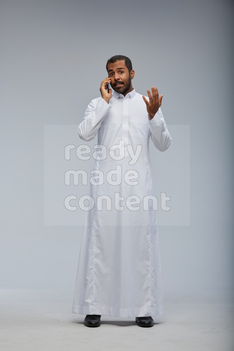 Saudi man wearing Thob standing talking on phone on Gray background