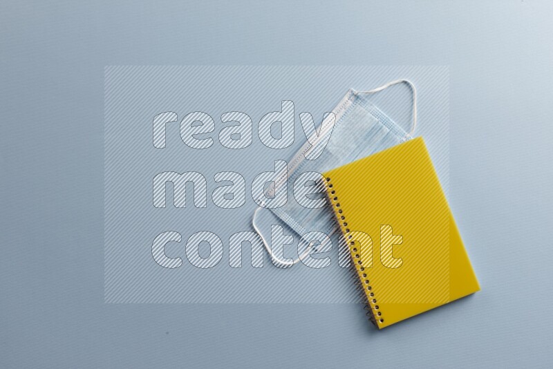 A yellow notebook with different school supplies on blue background