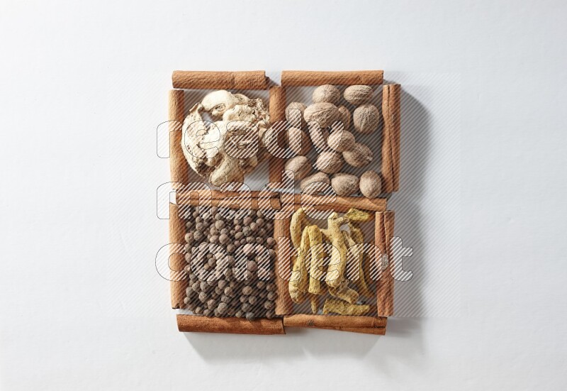 4 مربعات من أعواد القرفة ممتلئة بجوزة الطيب والزنجبيل المجفف وأصابع الكركم وبهار الفلفل الحلو على أرضية بيضاء