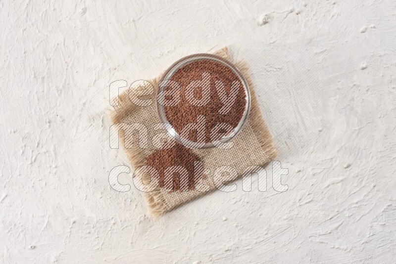 A glass bowl full of garden cress seeds on a burlap fabric on textured white flooring