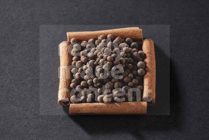 أربعة من أعواد القرفة مكونة شكل مربع بداخلها بهار الفلفل الحلو علي خلفية سوداء