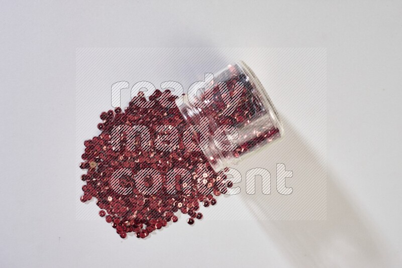 Colored flat sequins in a glass jar on grey background