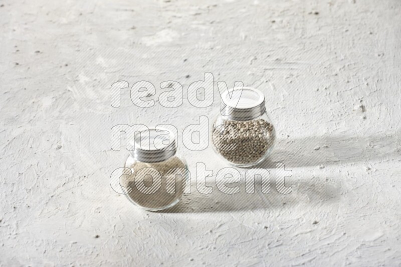 2 Herbal Glass jar full of white pepper beads and powder on textured white flooring