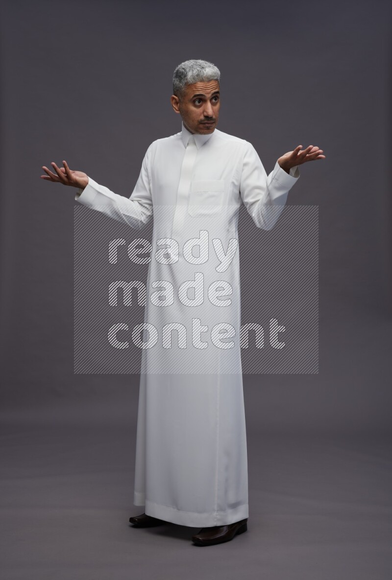 Saudi man wearing thob standing interacting with the camera on gray background