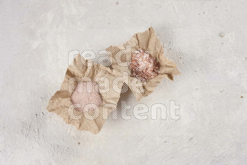 A crumpled piece of paper full of pink himalayan salt on white background