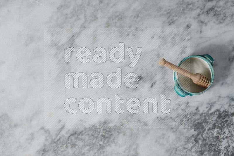 وعاء فخاري متعدد الألوان مع ملعقة عسل خشبية بداخله على خلفية من الرخام الرمادي