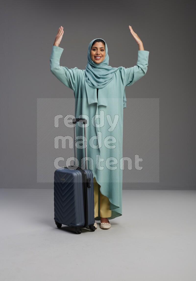 Saudi Woman wearing Abaya standing holding Travel bag on Gray background