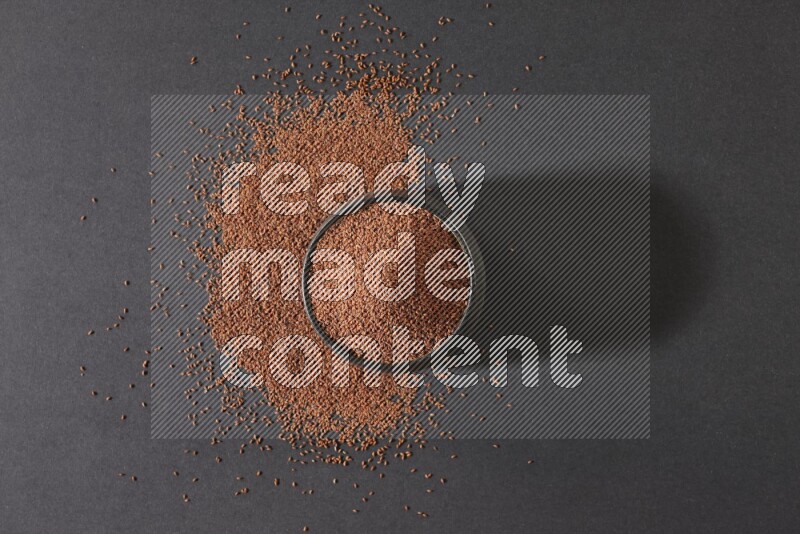 A black pottery bowl full of garden cress seeds surrounded by seeds on a black flooring