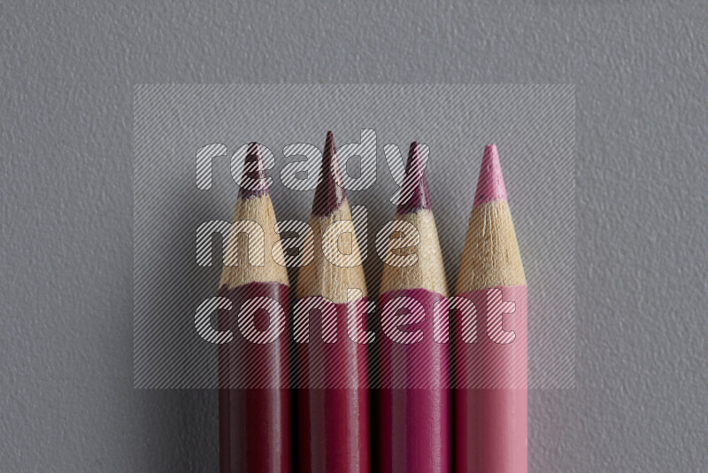 A collection of sharpened colored pencils arranged showcasing a gradient of pink hues on grey background