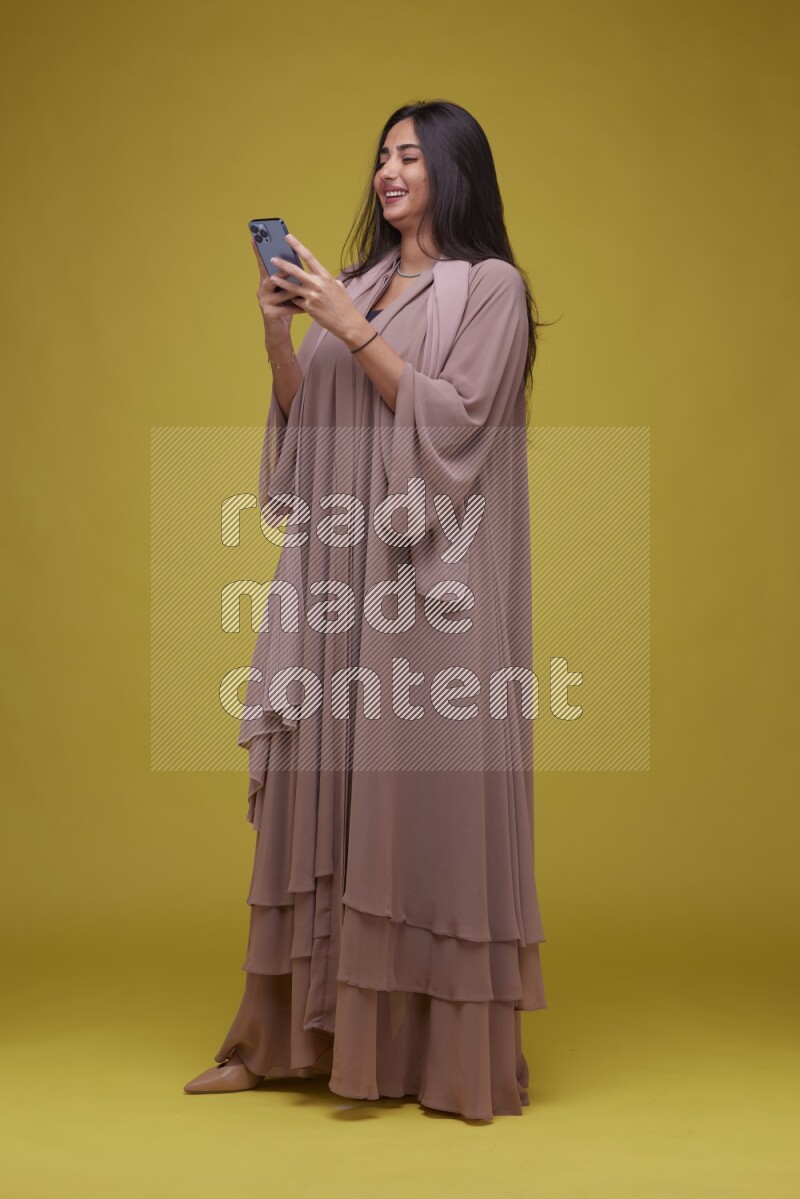 A woman Texting on a Yellow Background wearing Brown Abaya