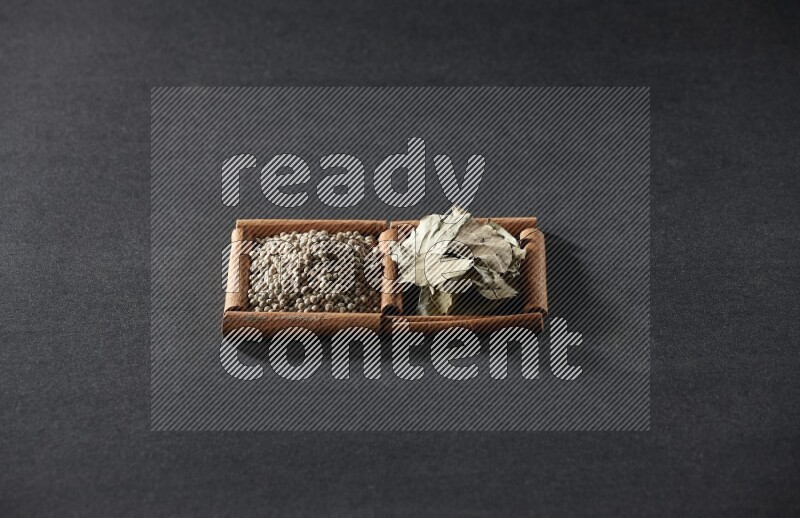 مربعان من أعواد القرفة ممتلئان بحبوب الفلفل الأبيض وأوراق الغار علي خلفية سوداء