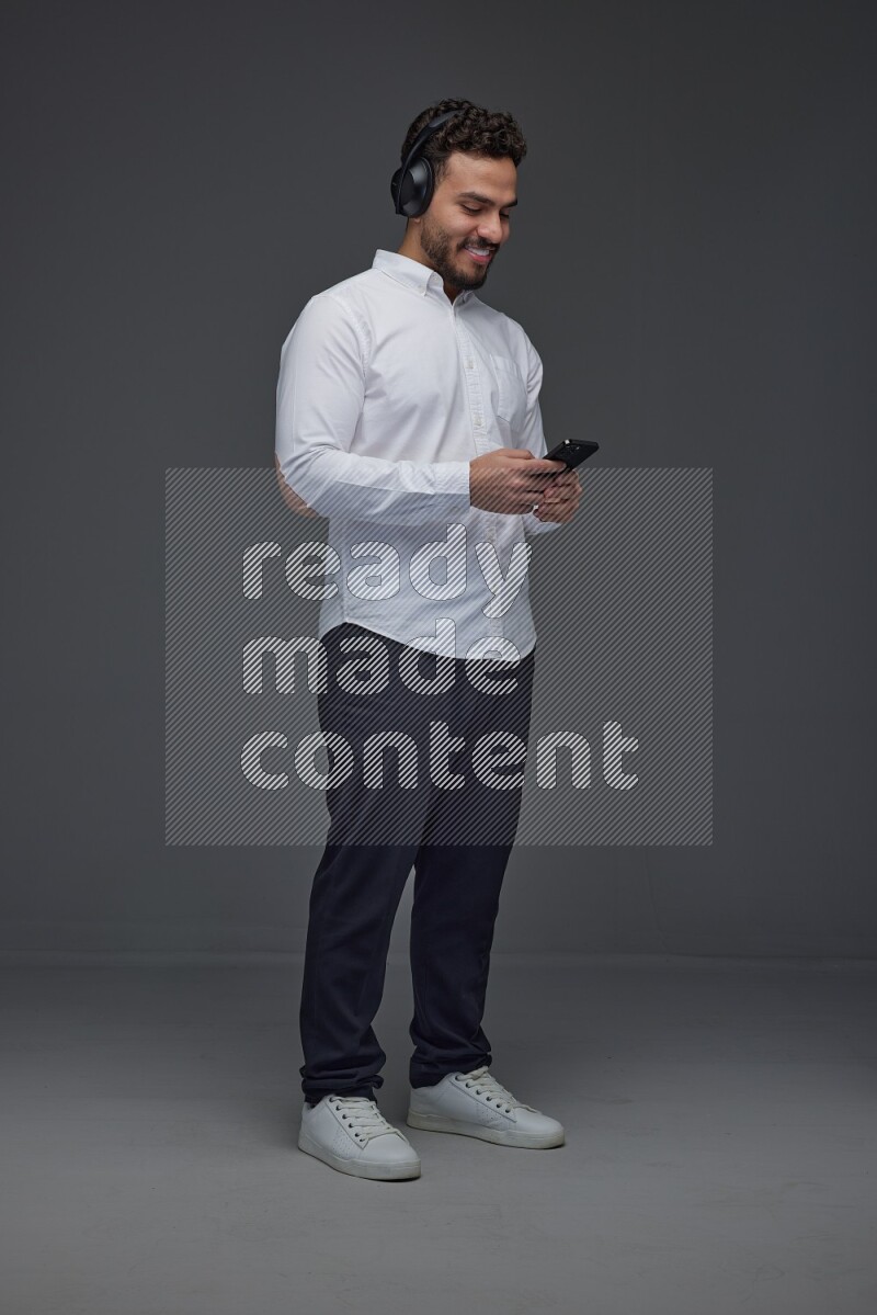 A man wearing smart casual and using his phone and headphone eye level on a gray background