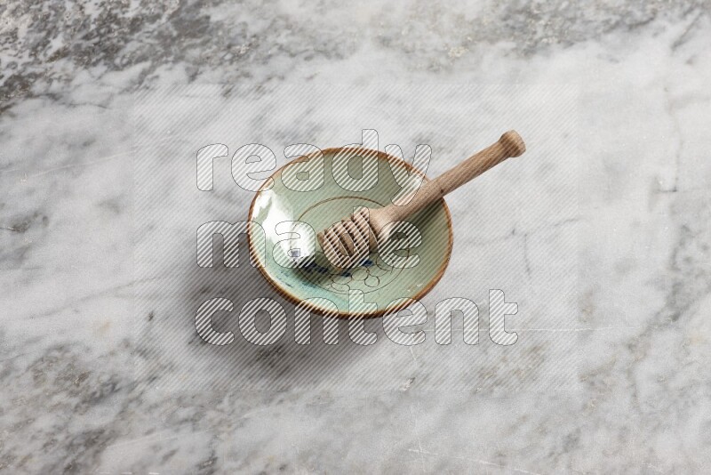 Decorative pottery plate with wooden honey dipper in it on grey marble background