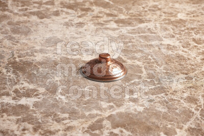 A small copper pot lid on beige marble background