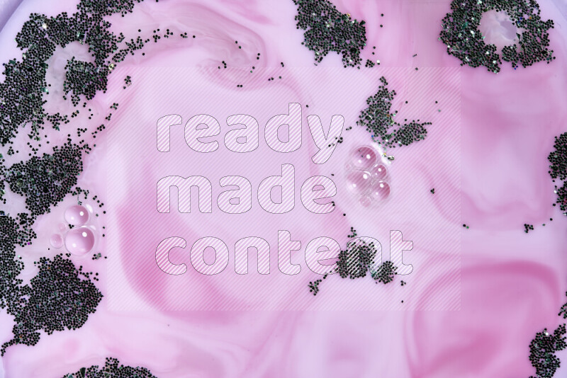 A close-up of sparkling green glitter scattered on swirling pink background