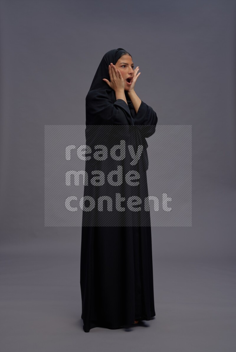 Saudi woman wearing Abaya standing hands behind head on gray background