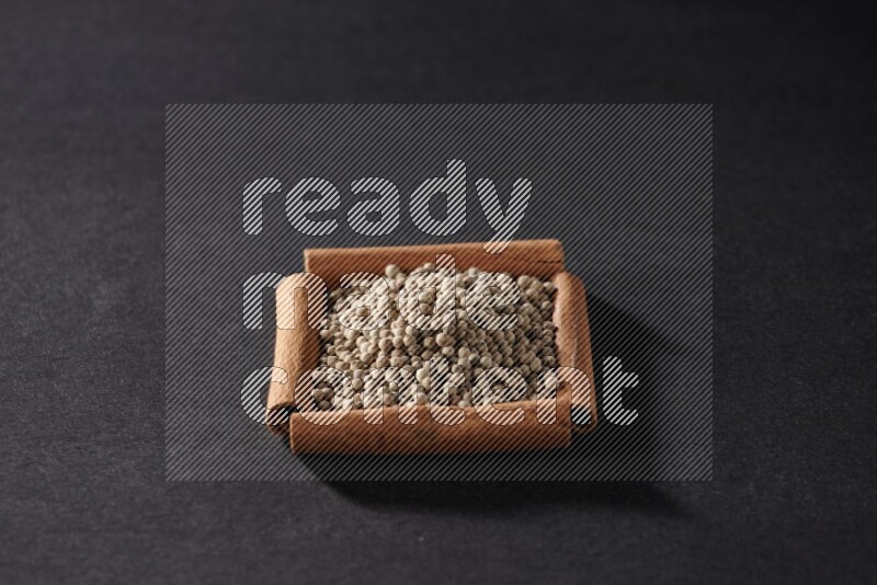 A single square of cinnamon sticks full of white pepper on black flooring