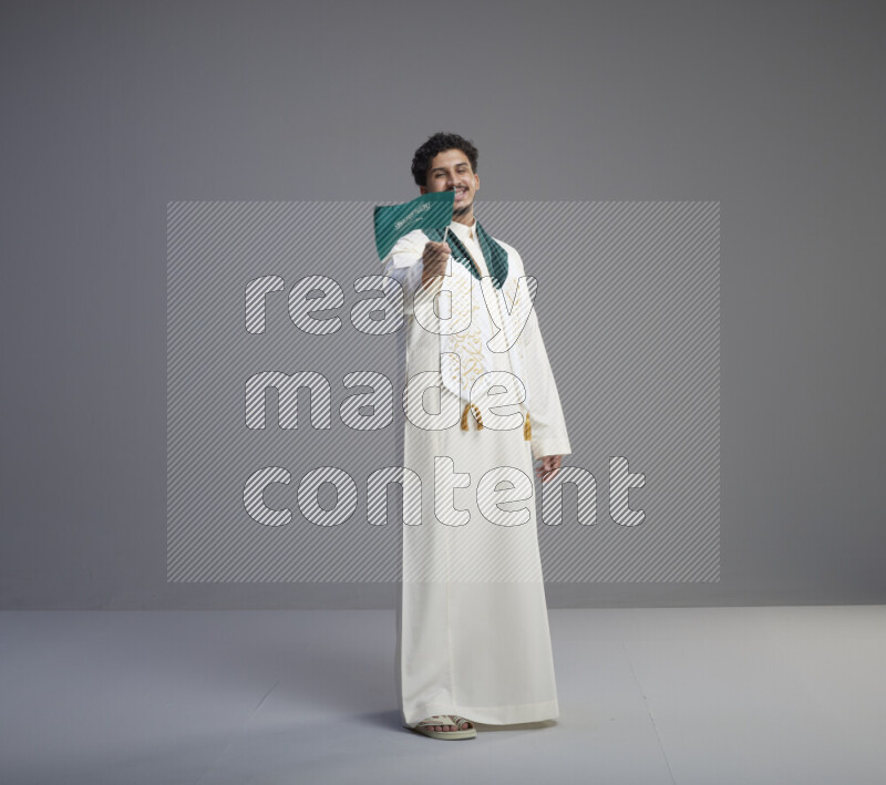 رجل سعودي يرتدي ثوب ابيض ويحمل علم السعودية