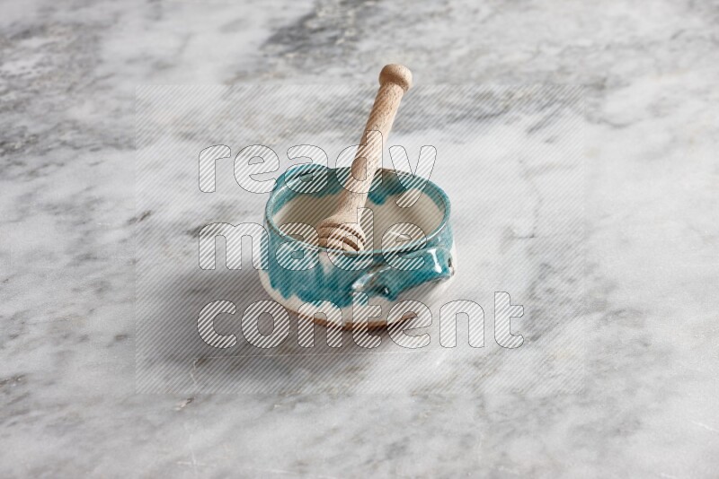 Multicolored pottery bowl with wooden honey dipper in it on grey marble background