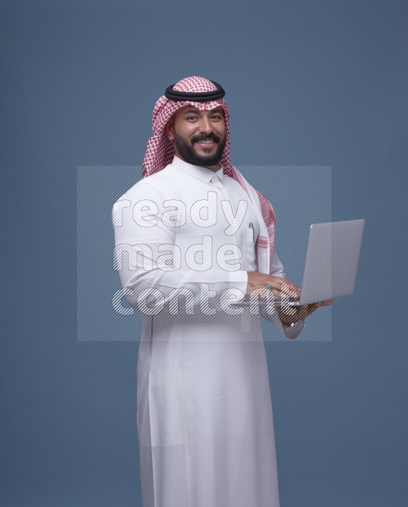 A Saudi man Holding a Laptop on Blue Background wearing Saudi Thob and Shomag