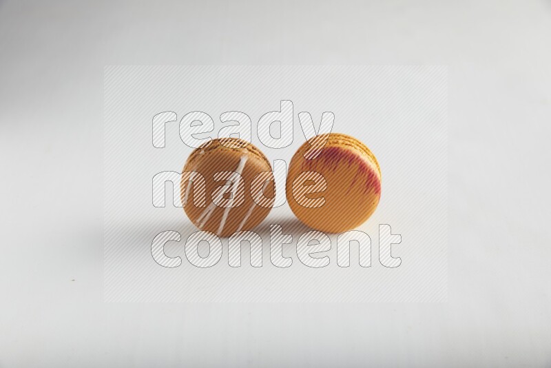 45º Shot of of two assorted Brown Irish Cream, and Orange Exotic macarons on white background