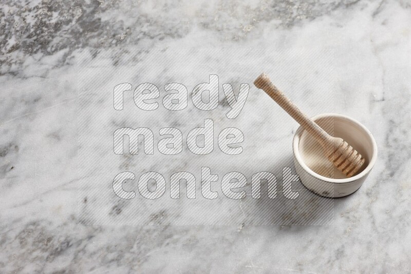 White pottery bowl with wooden honey dipper in it on grey marble background