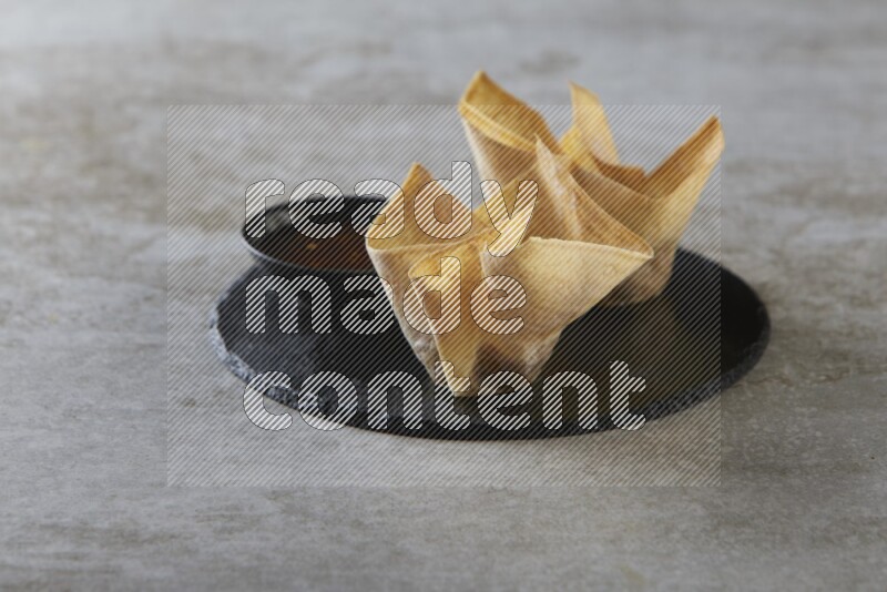 wonton cups with soy sauce ramkin on circle slate on grey textured counter top